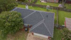 Aerial photo of a home with CertainTeed Landmark, Moire Black Shingles and green grass and a lush tree in the front yard no cars in the driveway by Sustainable Roofing a local Bryan Texas Roofer