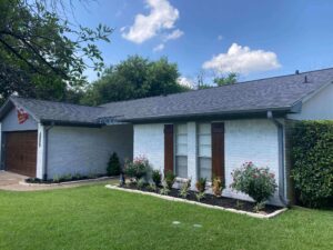 Side profile of a ranch style home in a light blue with Malarkey Highlander Storm Grey Shingles and fresh landscaping lush green grass and a clear blue sky with white puffy clouds in the background by Sustainable Roofing a College Station Roof Replacement Company