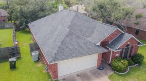 Side profile of a new Malarkey Products roof in weathered wood installed on a house with red brick and a white garage door by college station roofing company, Sustainable Roofing